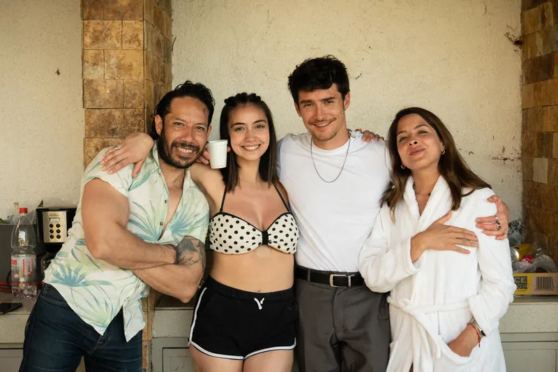 Four cast members hug and laugh on set